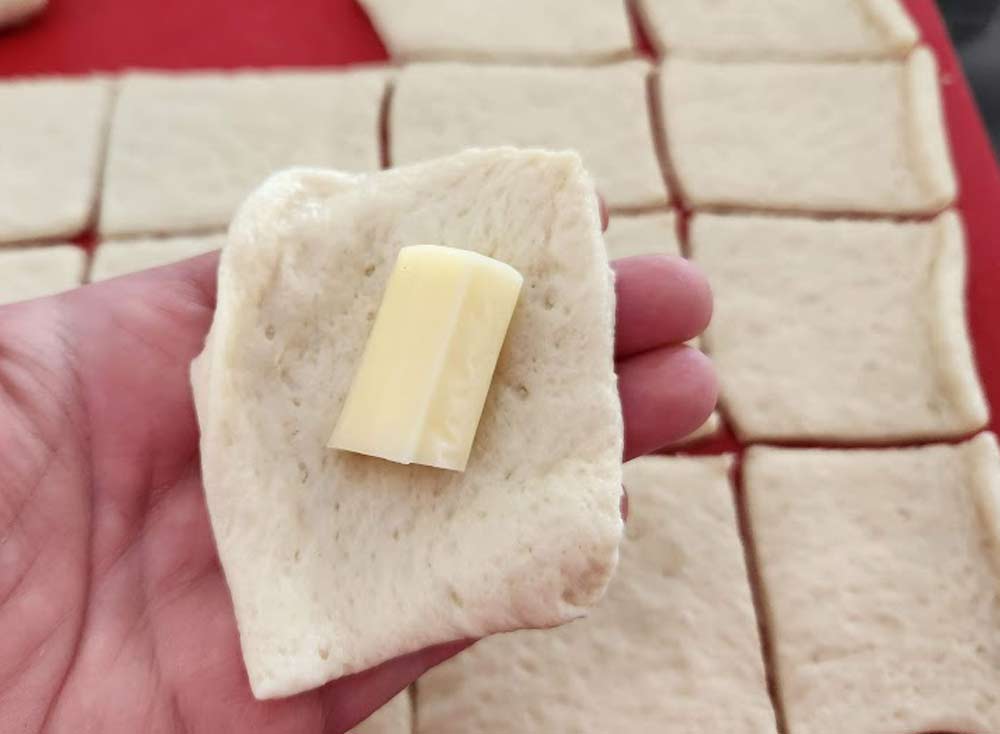 A square of dough with a piece of mozzarella cheese in the middle