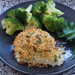 Finished parmesan crusted cod on a plate with steamed broccoli