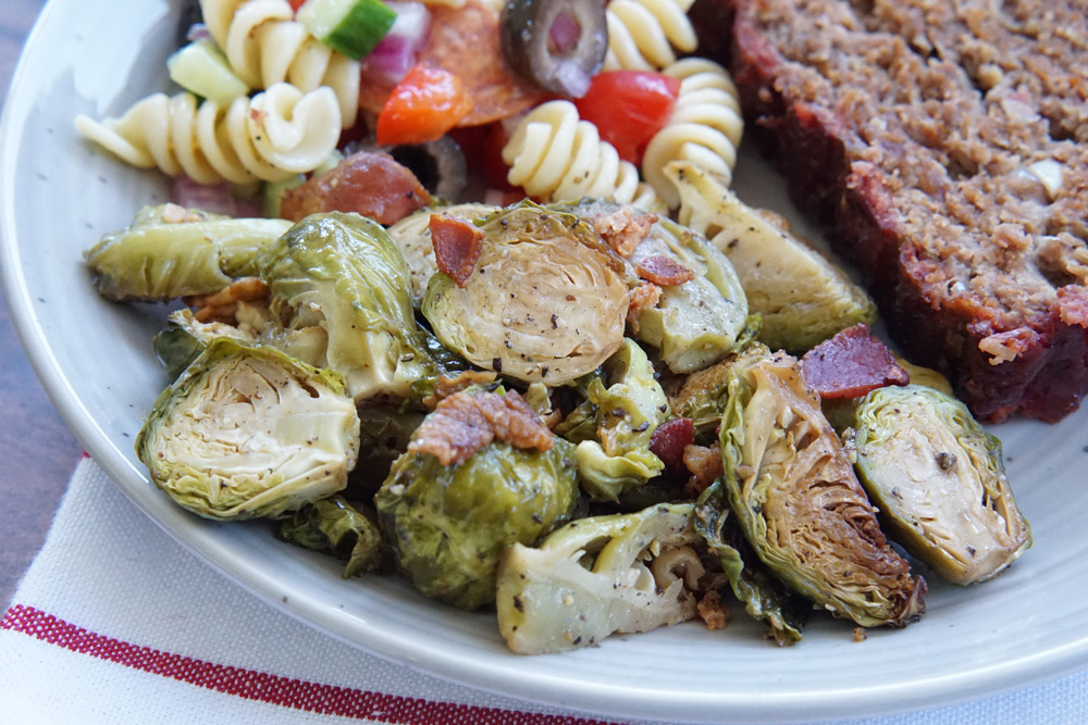 Smoked brussels sprouts on a plate with smoked meatloaf and pasta salad